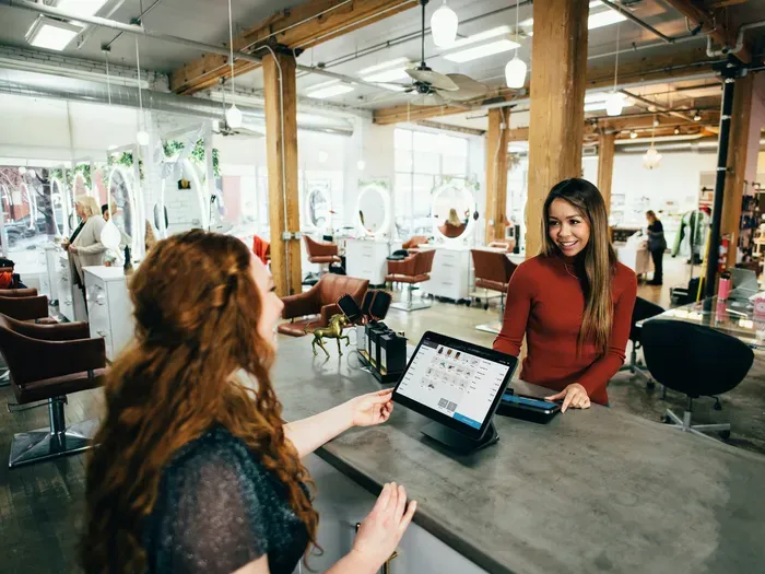 Friendly salon receptionist assisting a customer at the front desk with digital payment and booking system
